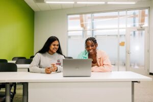 Women students working at desk in front of laptop.
